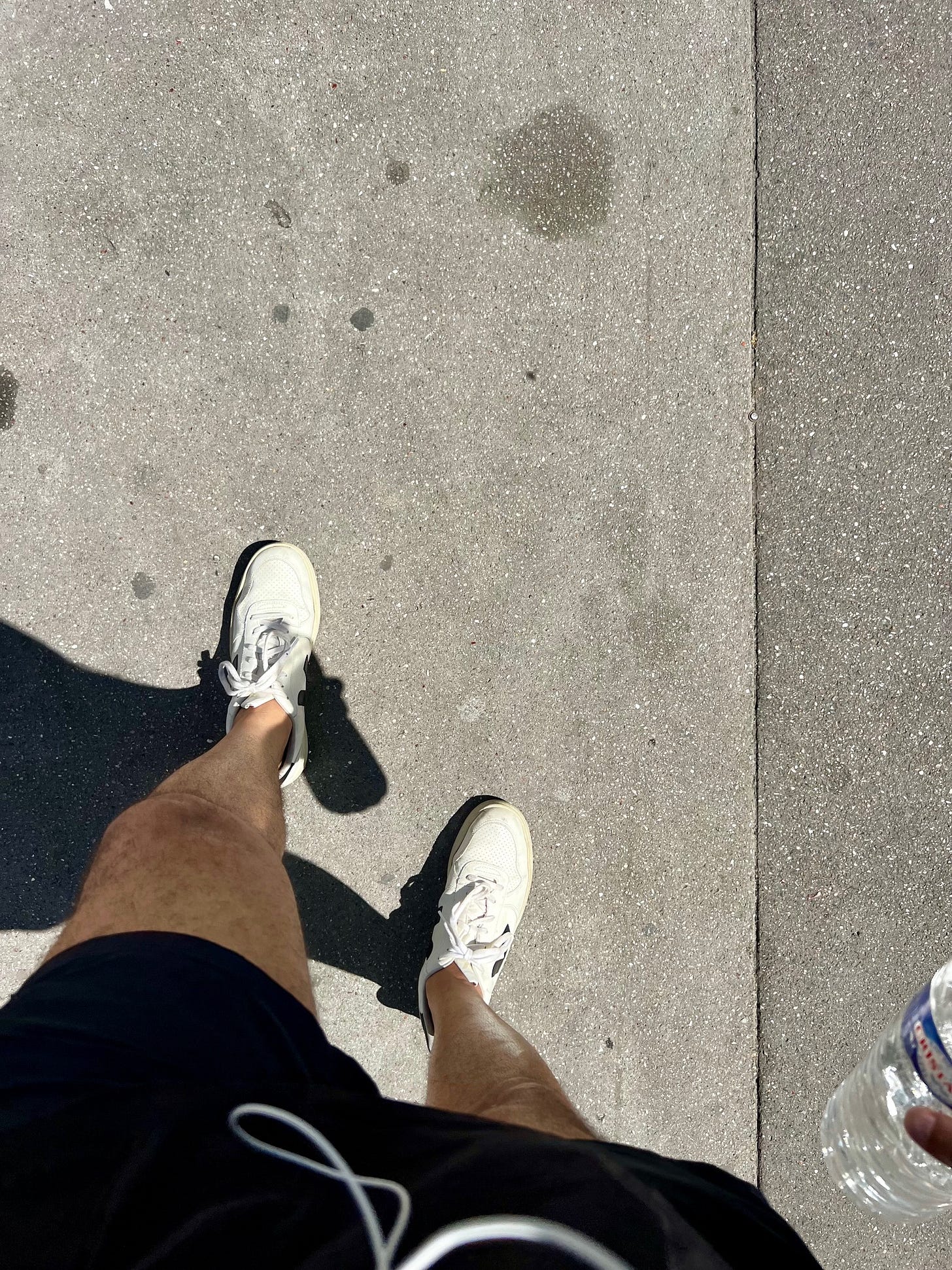 First-person view of feet in white sneakers walking on a Parisian sidewalk on a sunny day.