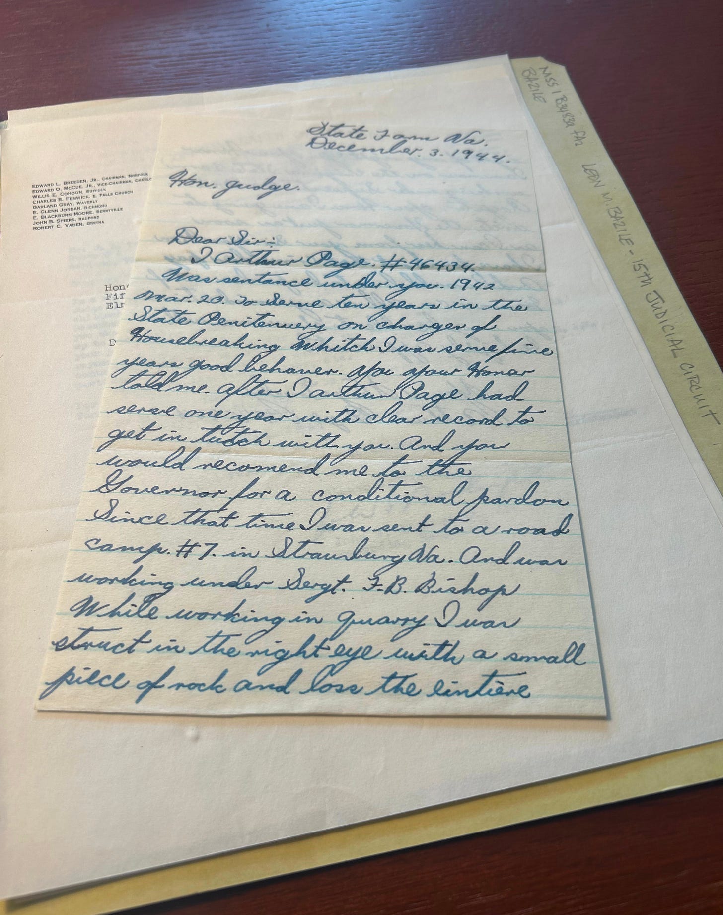 A handwritten letter from 1944 sits atop a pile of papers on a wooden desk.