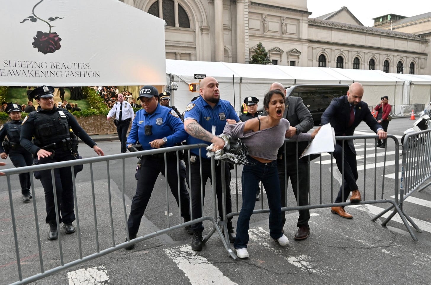 a group of police officers holding a young woman against a gate