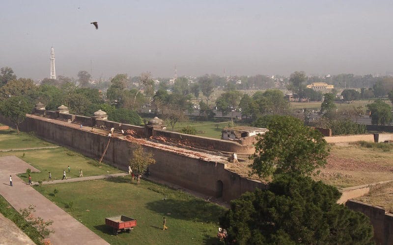 Photograph of dense smog over a fort wall and gardens in Lahore, Pakistan. In the foreground of the photograph, a bird flies through the smog.