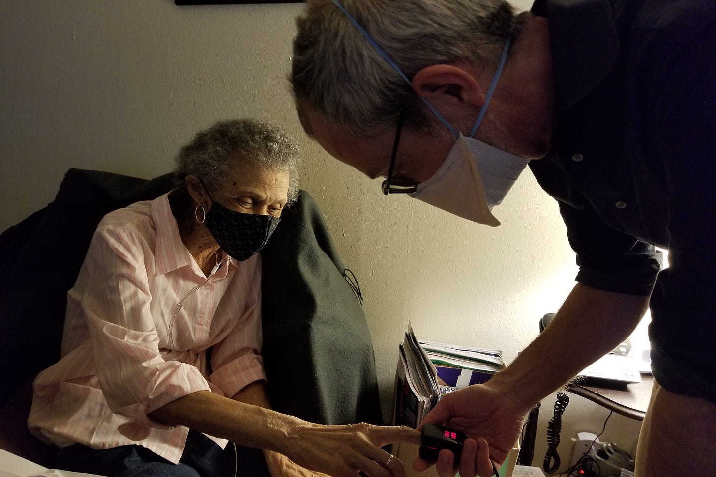 A doctor places a pulse oximeter on a senior woman's index finger. Both are wearing masks. A doctor places a pulse oximeter on a senior woman's index finger. Both are wearing masks.