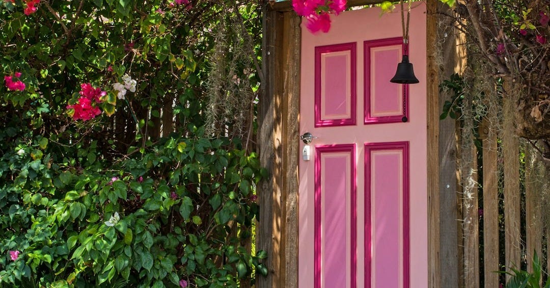 pink wooden door surround by flowers