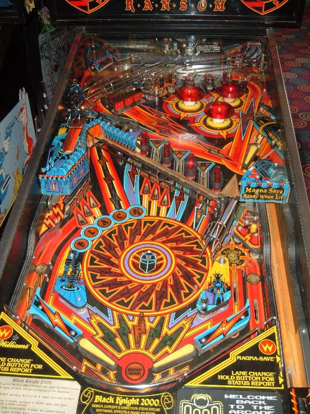 Black Knight 2000 (1989) playfield showing the electric-themed two-level layout with lightning bolt artwork, Magna-Save button, and 'RANSOM' text visible on the upper display Black Knight 2000 (1989) playfield showing the electric-themed two-level layout with lightning bolt artwork, Magna-Save button, and 'RANSOM' text visible on the upper display
