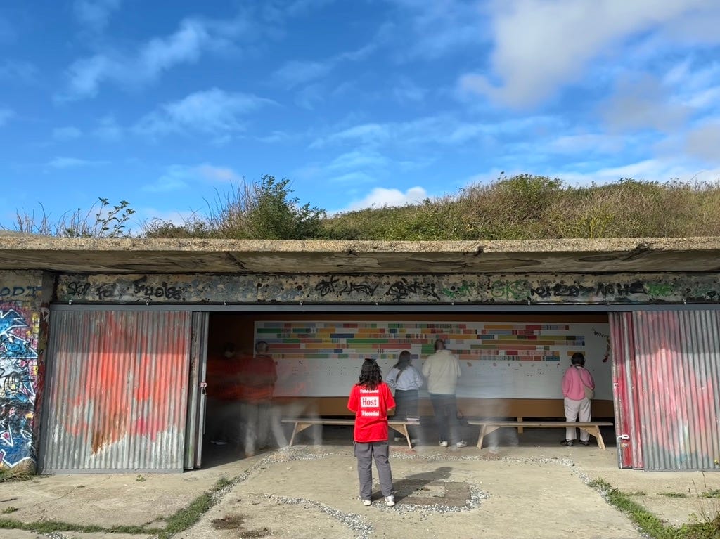 A volunteer in scarlet red t-shirt stand with their back to us in front of a temporary sound installation inside an old cliff edge bunker that has concrete walls and a flat concrete roof, part of the Folkestone Triennial. A volunteer in scarlet red t-shirt stand with their back to us in front of a temporary sound installation inside an old cliff edge bunker that has concrete walls and a flat concrete roof, part of the Folkestone Triennial.
