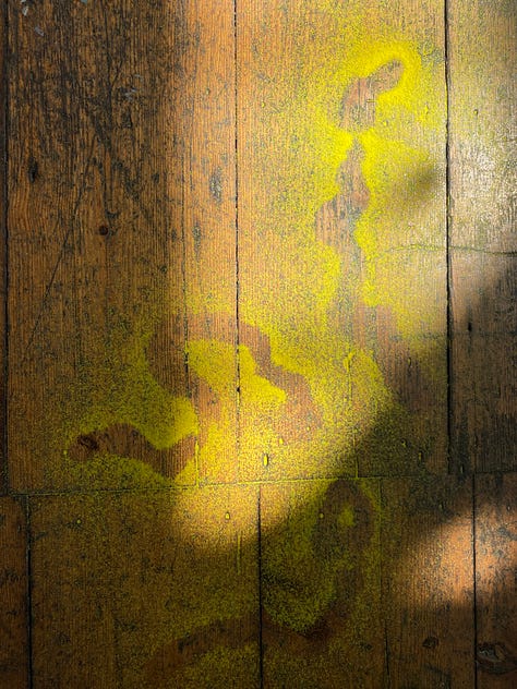 1: a wooden table featuring a selection of tools for mark-making and drawing. 2: a selection of abstract drawings featuring figures and stones in earthy tones. 3: a wooden floor covered in twirling patterns of yellow sand.