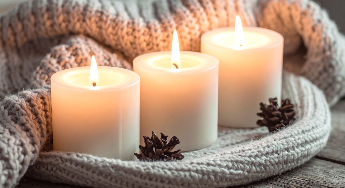 Three candles nestled in a grey knitted blanket