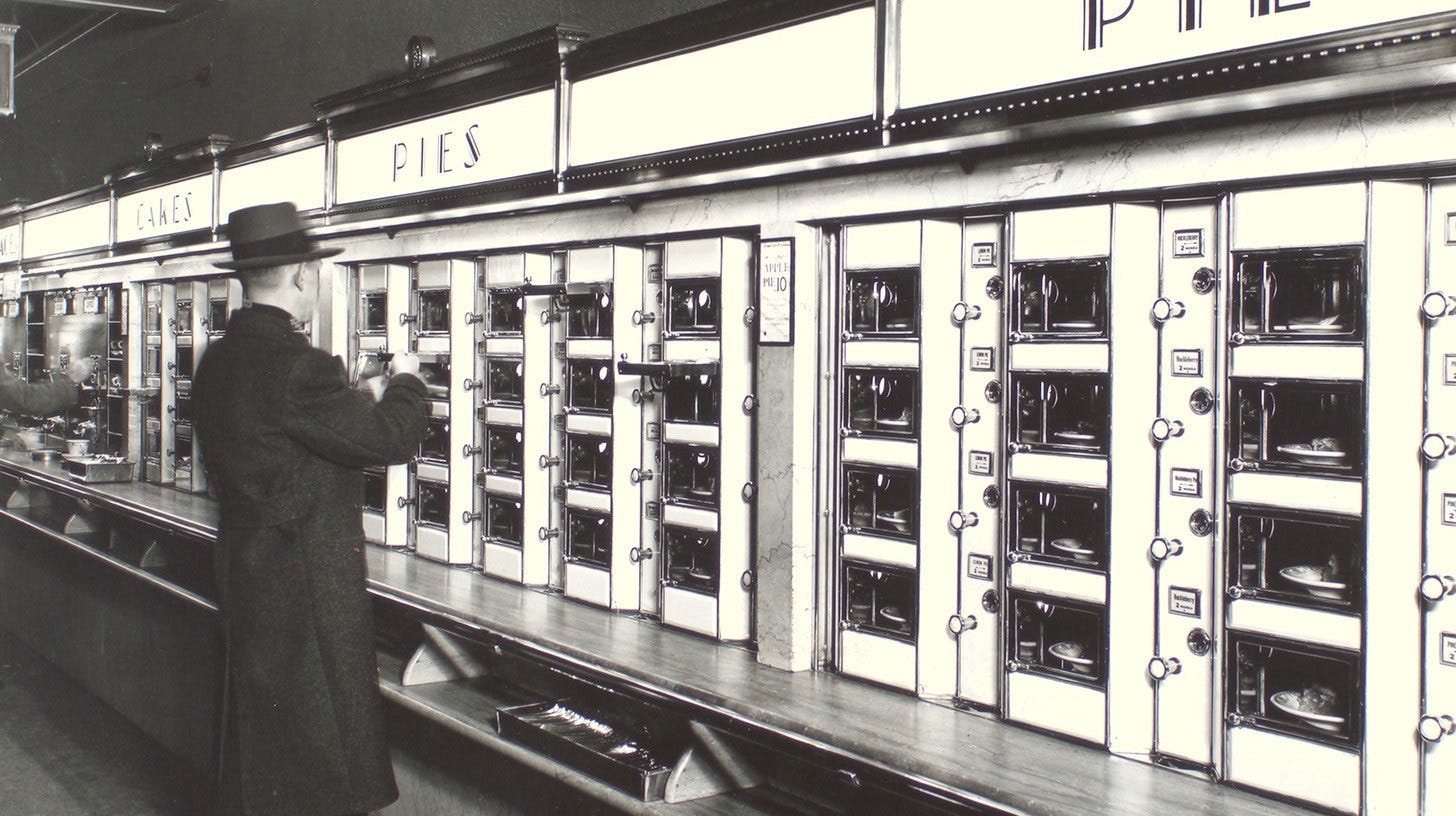 A man in a hat and long coat stands before the Automat’s wall of small coin-operated glass doors filled with pies, beneath PIES and CAKES signs, New York, 1936 A man in a hat and long coat stands before the Automat’s wall of small coin-operated glass doors filled with pies, beneath PIES and CAKES signs, New York, 1936