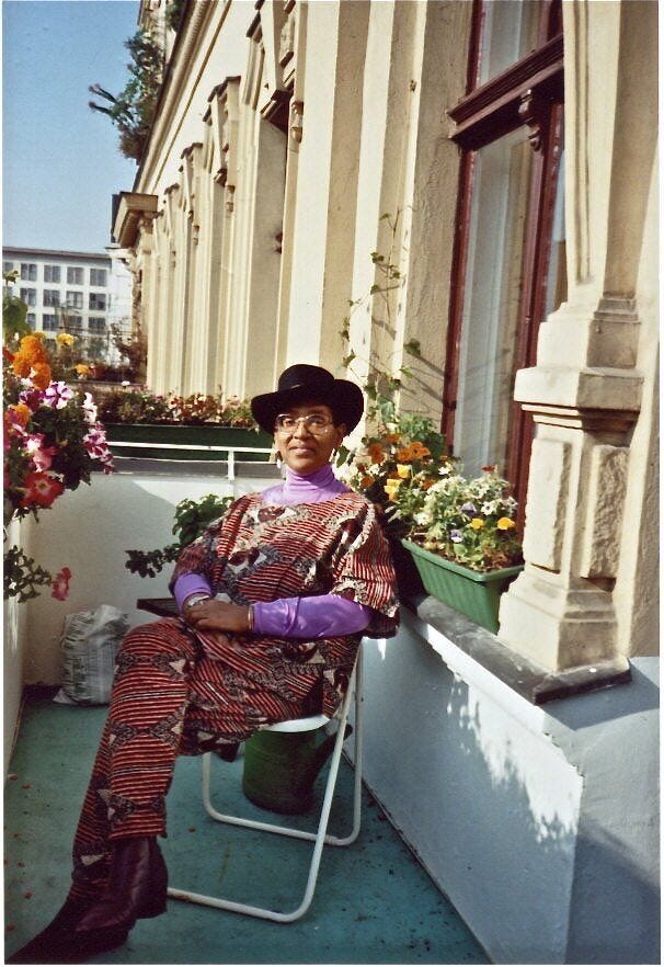 This may contain: a woman sitting on a chair in front of a building with flowers and potted plants