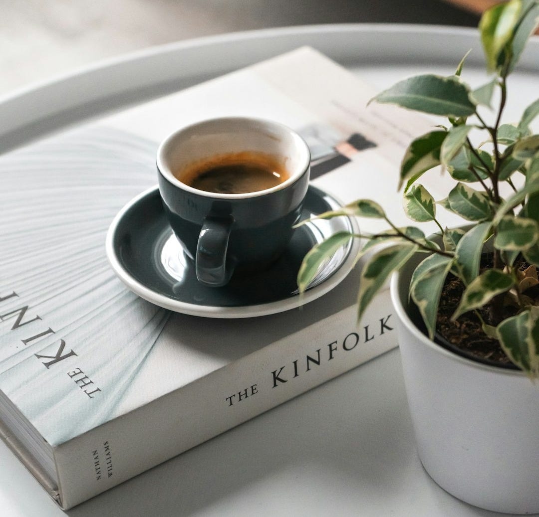 shallow focus photo of black ceramic mug and saucer on white book shallow focus photo of black ceramic mug and saucer on white book