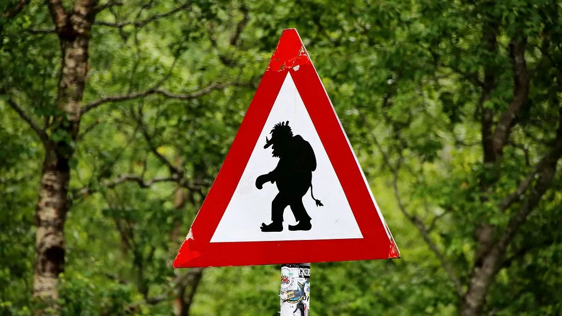 A white triangle warning sign with red border showing the silhouette of a troll