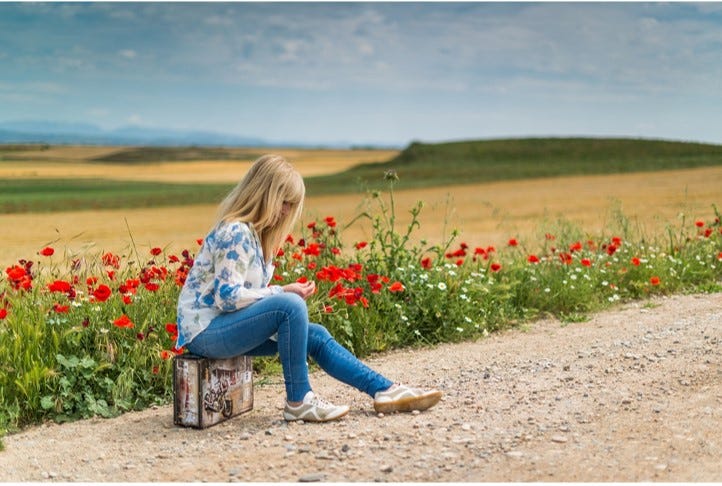 Young girl sitting on a suitcase by the side of a dusty road