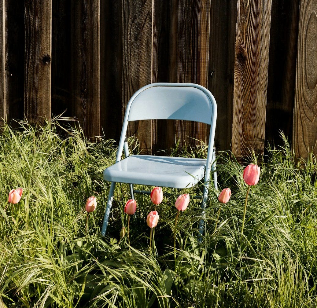 a blue chair sitting in tall grass next to a fence