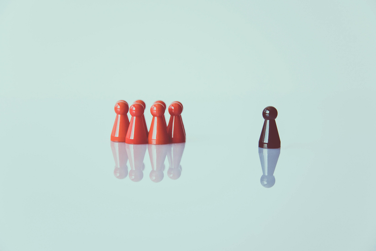 Free Red game pieces grouped with one isolated piece symbolizing social distancing on a reflective surface. Stock Photo Free Red game pieces grouped with one isolated piece symbolizing social distancing on a reflective surface. Stock Photo