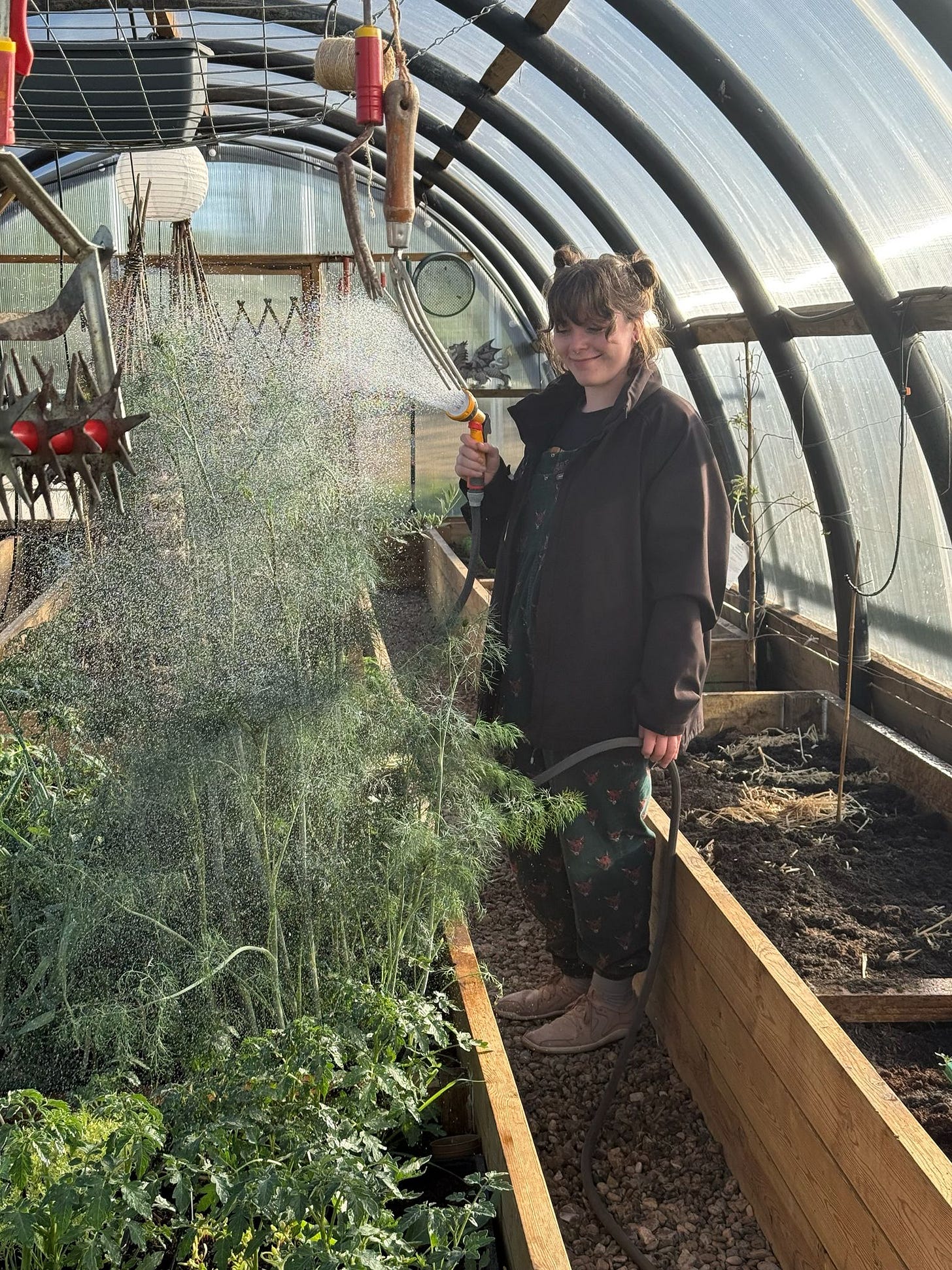 photo of Rhian in a polytunnel watering vegetables. She looks happy. photo of Rhian in a polytunnel watering vegetables. She looks happy.