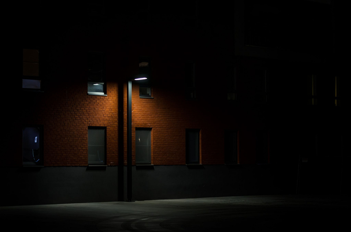 A dark street with a single streetlight shining on part of a brick building, while the rest stays in shadow.