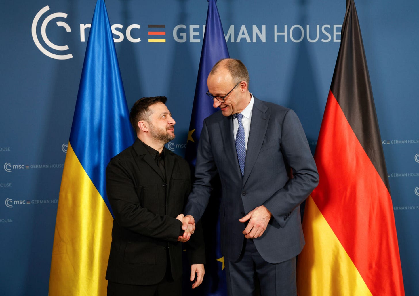 Two men shaking hands in front of flags

AI-generated content may be incorrect.
