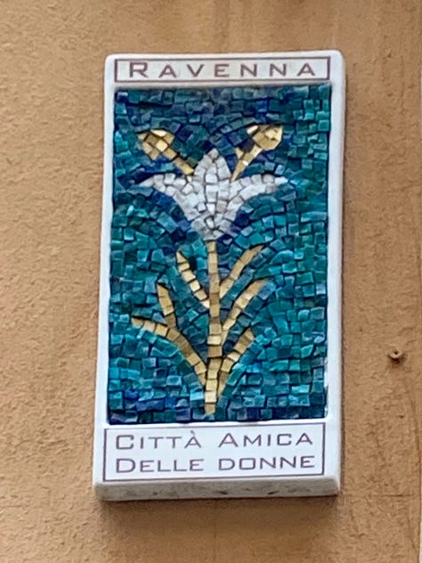Three mosaic flower wall-plaques depicting a white lily, a white tulip and a poppy, with text declaring Ravenna to be a city friendly to women.