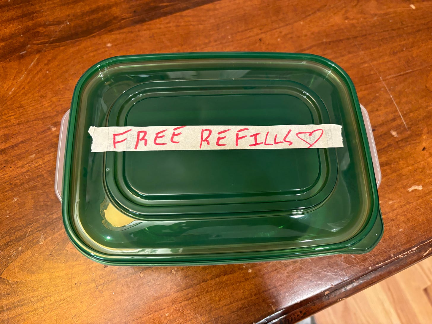 A green rectangular Tupperware with FREE REFILLS written in red on masking tape in messy handwriting