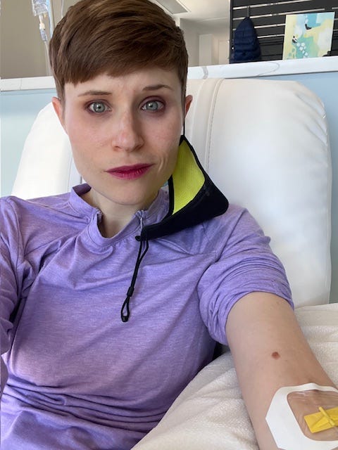 Selfie of OP in infusion chair with IV in left arm. She appears as she did in the 2nd photo, but now her mask is hanging from one ear, exposing her face. Selfie of OP in infusion chair with IV in left arm. She appears as she did in the 2nd photo, but now her mask is hanging from one ear, exposing her face.