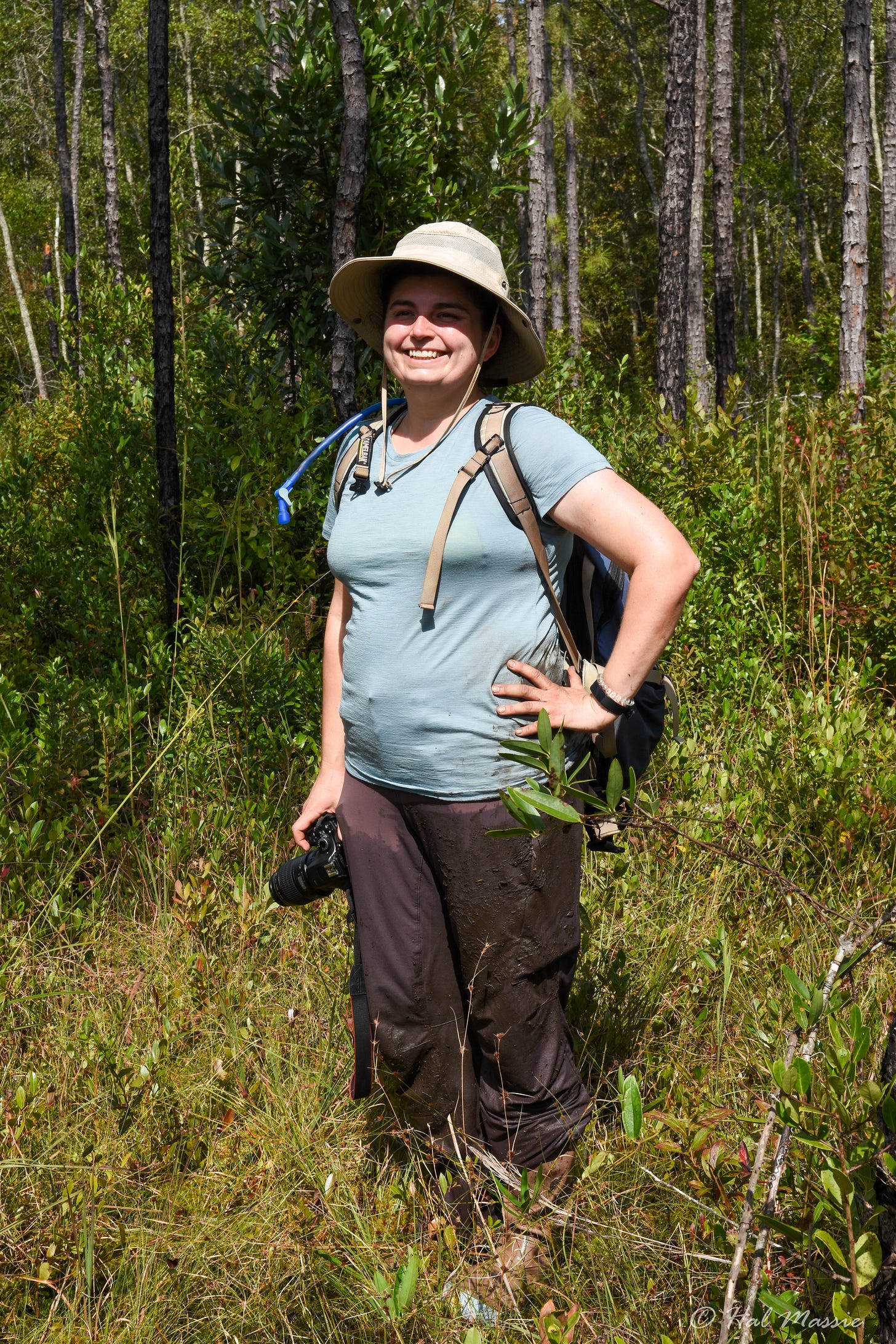 The author, a white woman, standing outside smiling, wearing wet, muddy hiking clothes