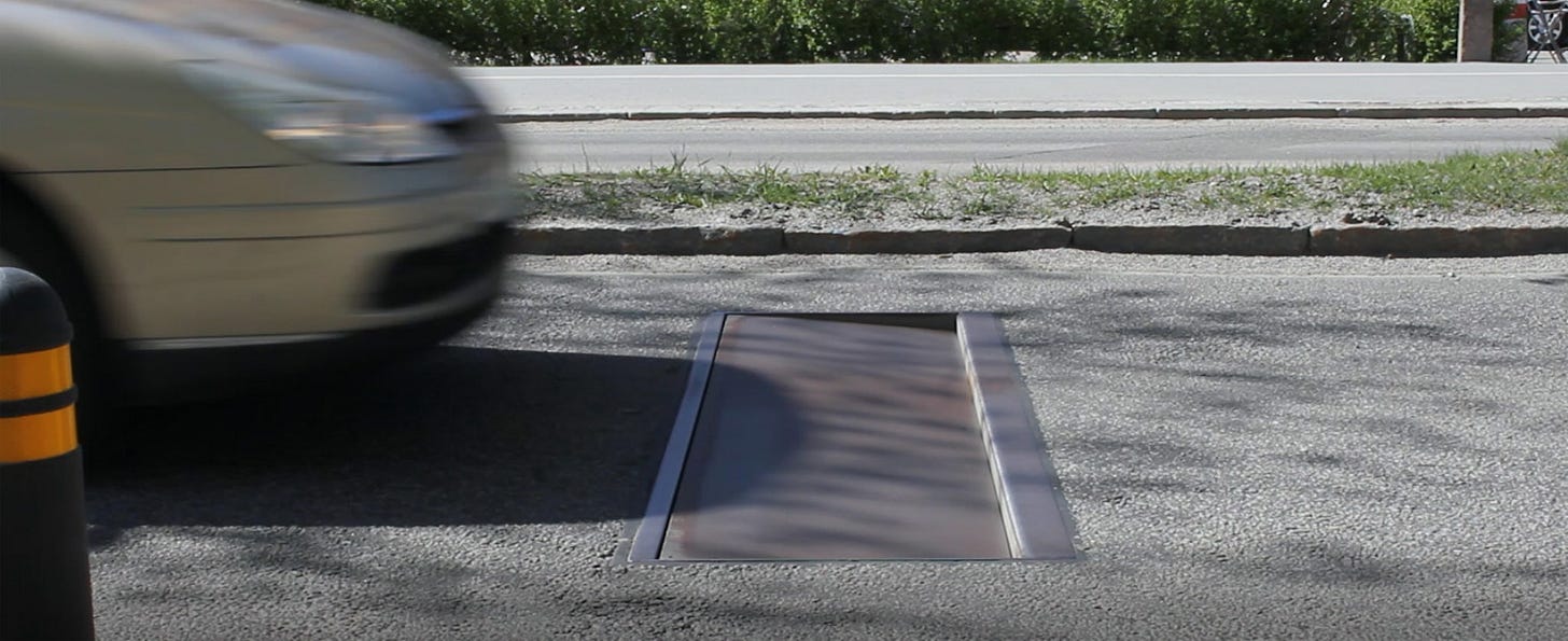 A photo showing Edeva's Actibump — it's a metal rectangular insert in the pavement, angled down to create a speed bump for a speeding car A photo showing Edeva's Actibump — it's a metal rectangular insert in the pavement, angled down to create a speed bump for a speeding car