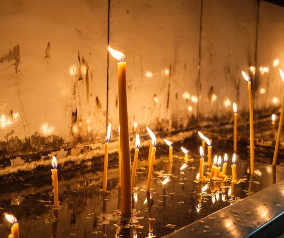 Tall and slender candles burning in rows, their reflections flickering in melted wax.