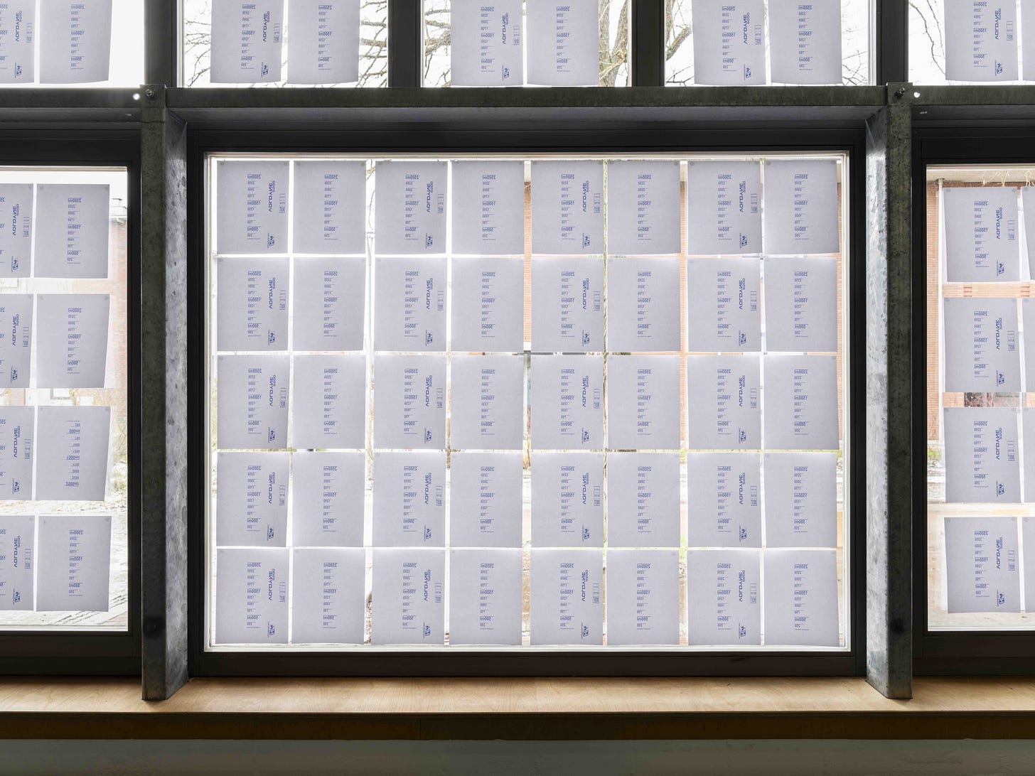 White printer paper with blue text is hanging in large windows. Made for remote viewing over Zoom, the narrative transports the audience to the icy grounds of the university, conveying each embodied detail: ‘I move carefully, as it is slippery. … I breathe in the ice-cold air. When I breathe out, a small cloud appears. Both my body and the air flowing out of my lungs are warmer than all that surrounds me.’