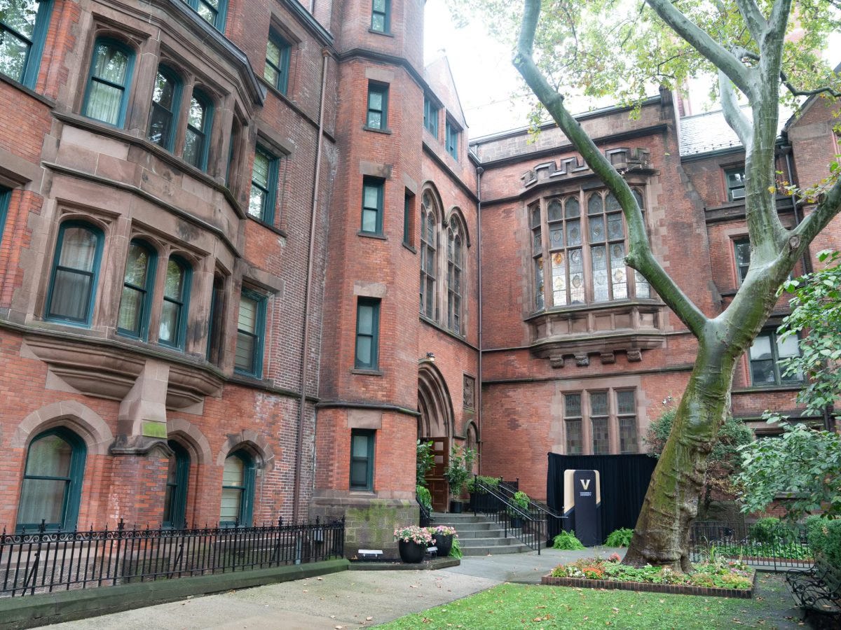 A regal red and brown stone academic building with pristine courtyard and tree in front, including a small sign with Vanderbilt's logo