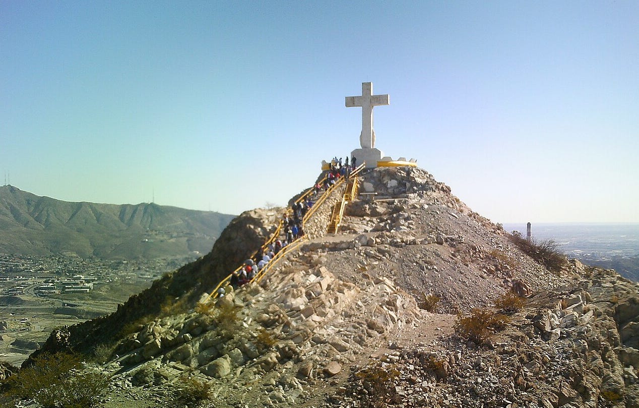 Dozens of people climb stairs on a mountain as they make their way to a large stone cross overlooking a city Dozens of people climb stairs on a mountain as they make their way to a large stone cross overlooking a city