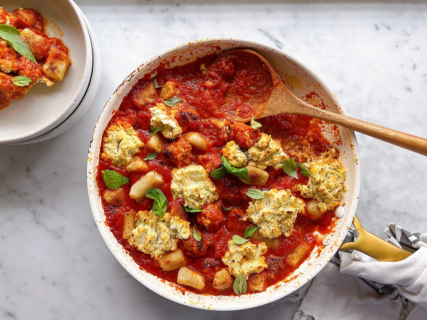 Photo of saucy meatballs and gnocchi in a skillet with some dished up in a bowl next to it and topped with basil