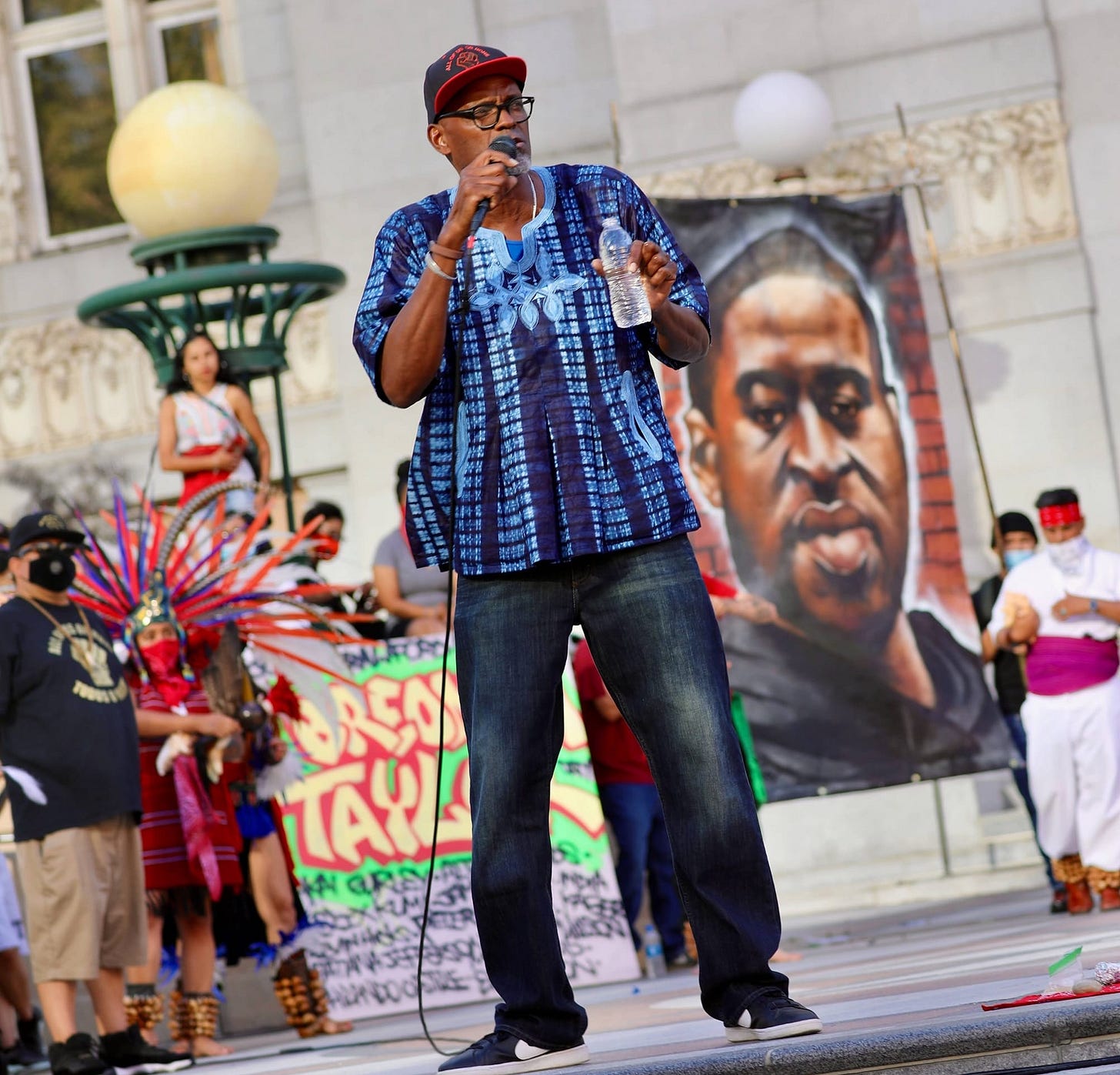 Greg in a blue African shirt pouring libation at a rally for George Floyd and Breonna Taylor