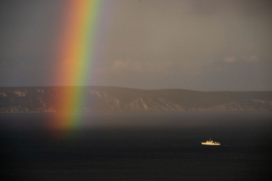 A distant view of a ship sailing near the end of a rainbow