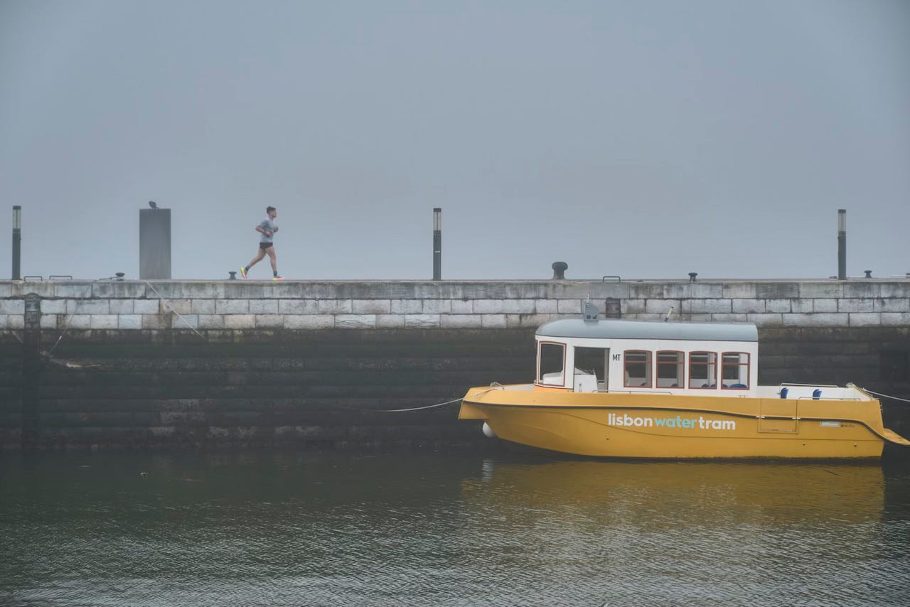 A yellow boat moored in the docks in Lisbon, with a person running in the background, in a morning fog A yellow boat moored in the docks in Lisbon, with a person running in the background, in a morning fog