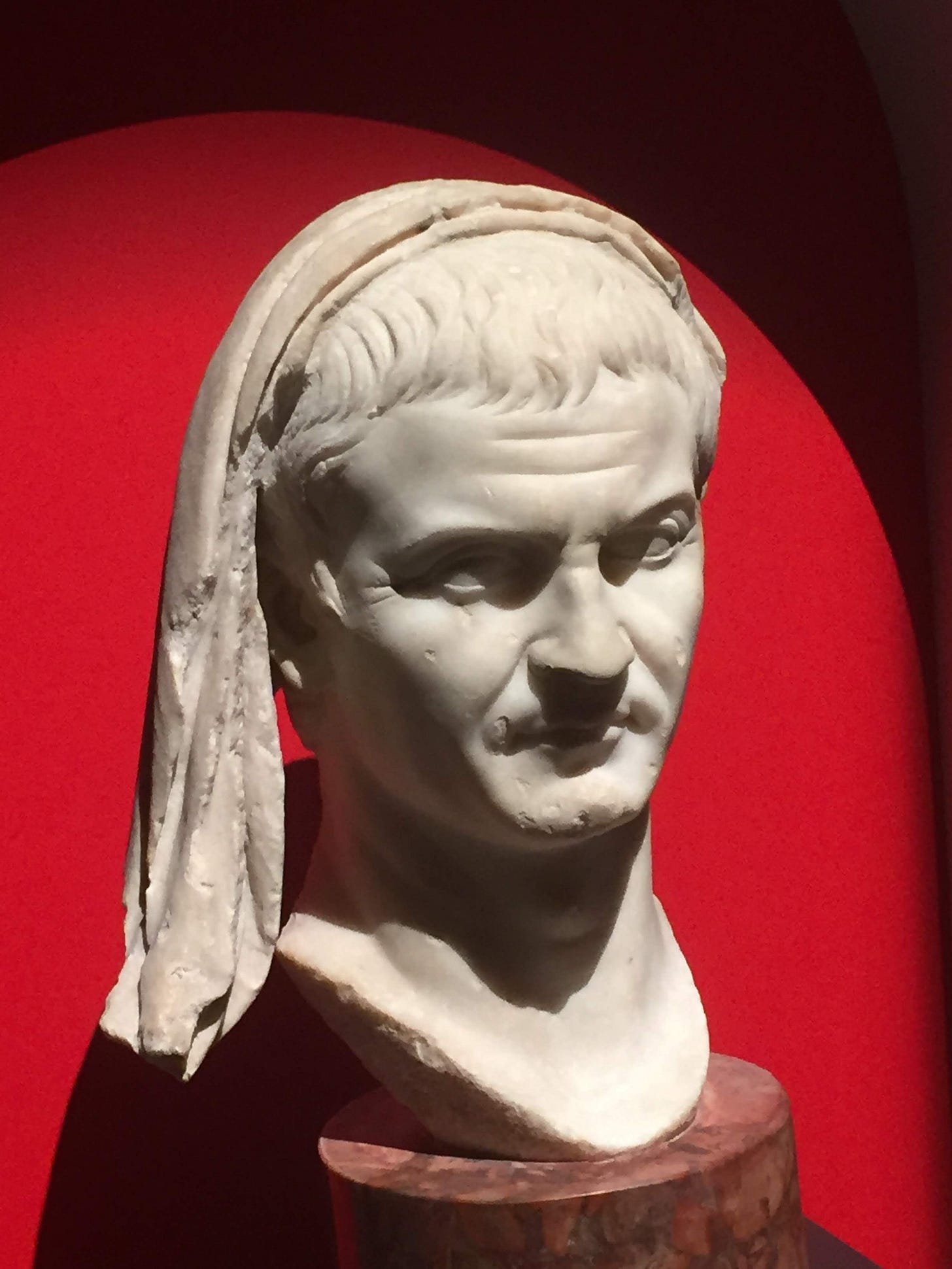 marble bust of a ROman, with a fold of his toga drawn over his head: red background marble bust of a ROman, with a fold of his toga drawn over his head: red background