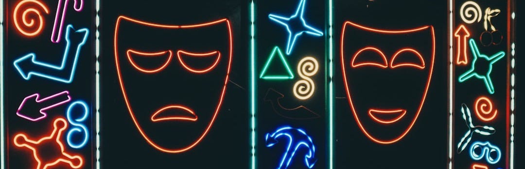 Neon signs depict happy and sad theater masks.