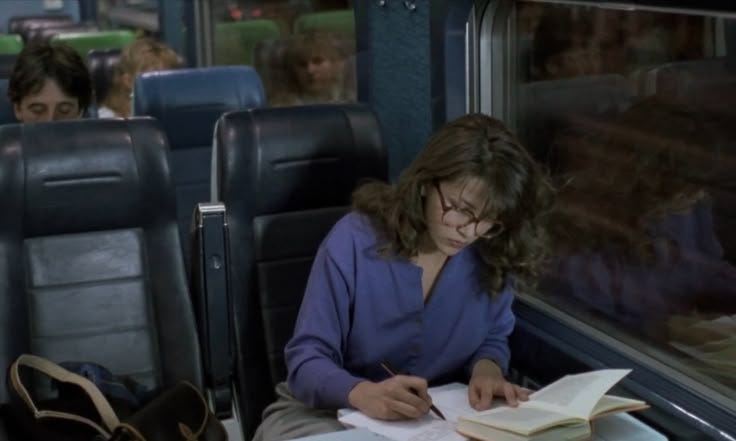 This may contain: a woman sitting on a train with a book and pen in her hand as she writes