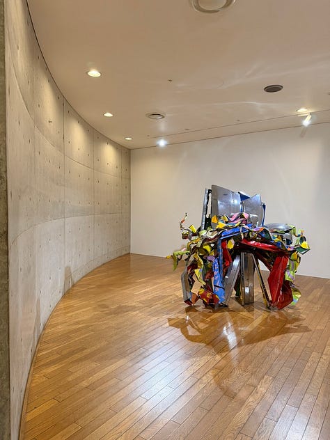 A grid of nine images depicting artworks by various artists, including Bruce Nauman, Jannis Kounellis, John Chamberlain, Yves Klein, Louise Nevelsen, Jenny Holzer, and Kan Yasuda.