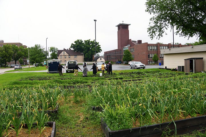 Image 1: A large open area of green grass in front of a parking lot. Image 2: A multirow garden with raised beds and boxes in front of a parking lot.