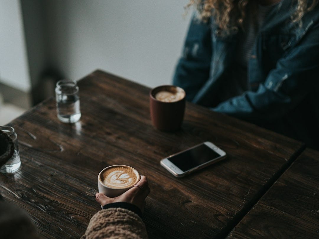 person in brown sweater holding cup while sitting in front of table inside room