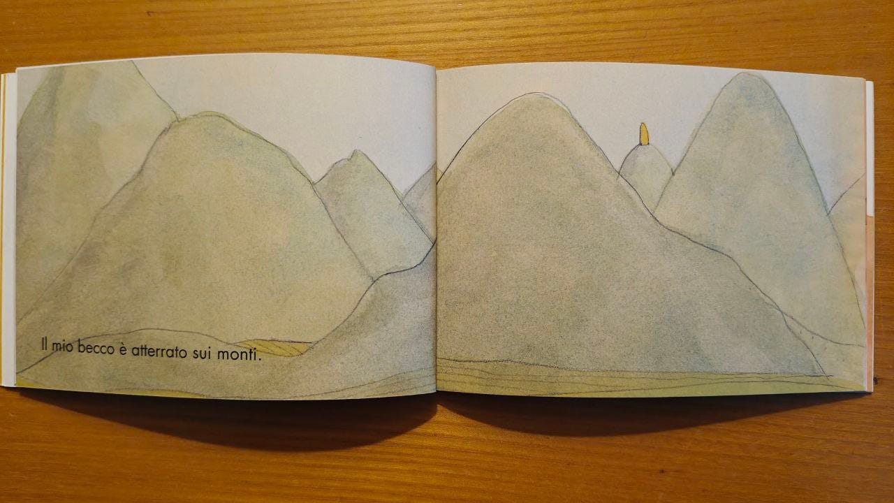 Due tavole dell'albo illustrato "Urla di mamma" appoggiato su un tavolo di legno: Sulle due pagine compaiono montagne verdi e sulla vetta di una c'è un becco di pinguino; nella pagina di sinistra c'è anche la scritta 'Il mio becco è atterrato sui monti.'