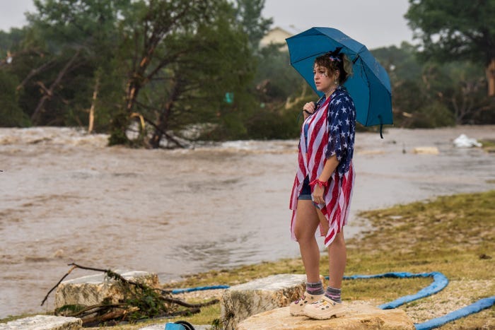woman in american flag outfit holding an umbrella watches flooding.