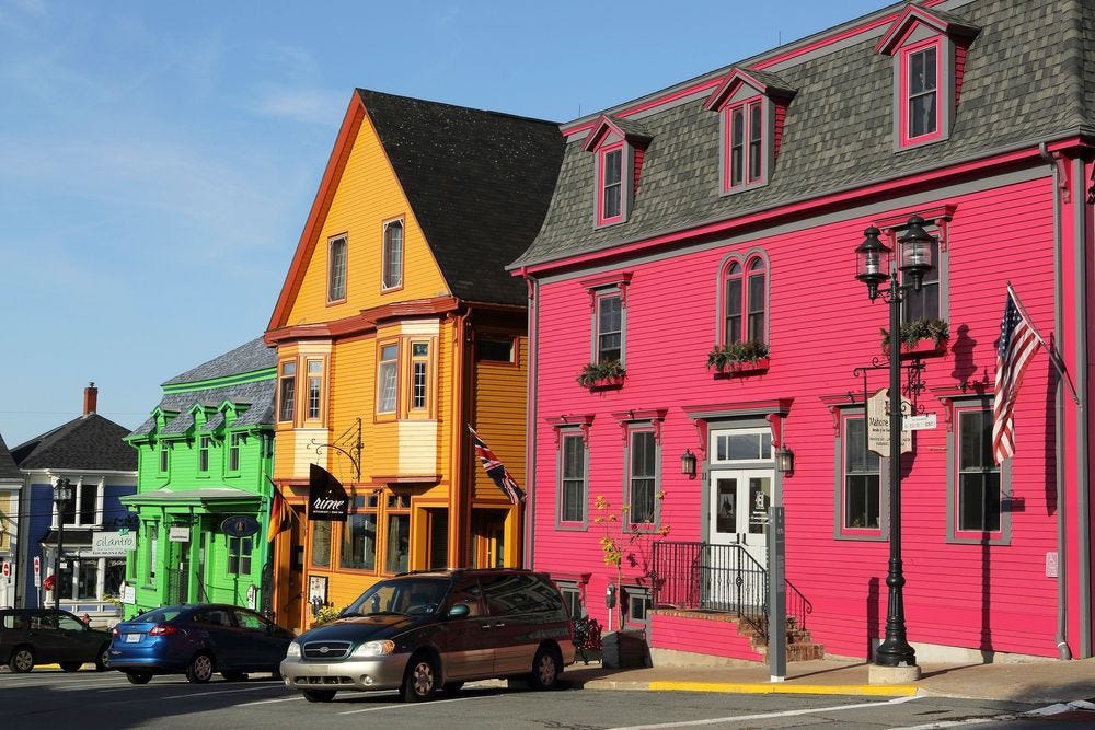A green house, a yellow house, and a red house on a row in a street.