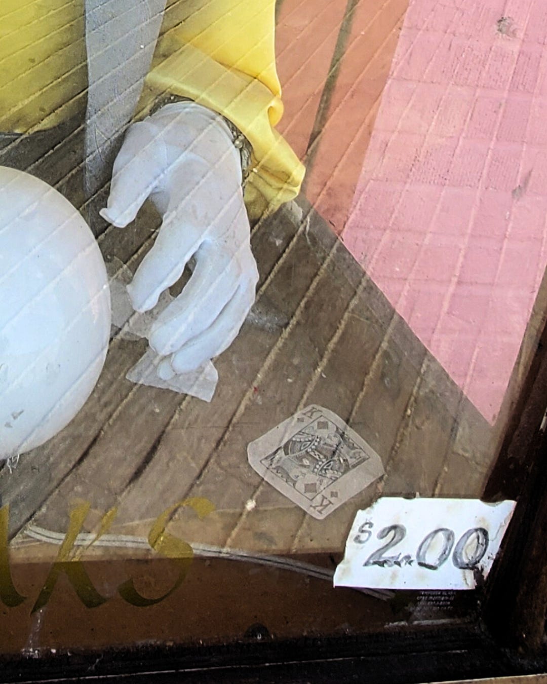 A white gloved hand hovers next to a plastic “crystal” ball. A King of Diamonds playing card lays on the surface next to it. There is a sign on the class declaring $2.00 in hand-written numerals.