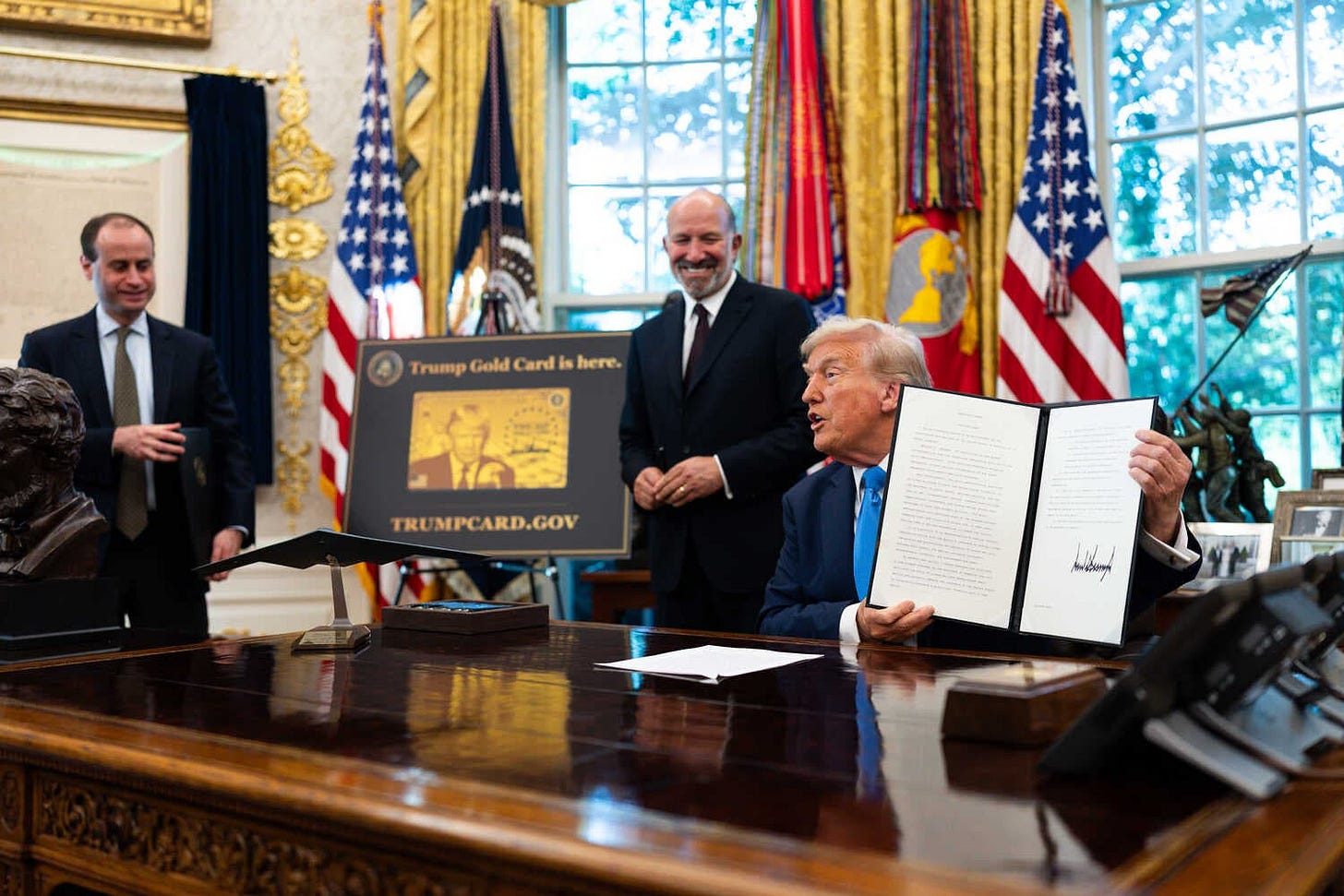 President Trump, sitting at a big desk, holds up the proclamation. President Trump, sitting at a big desk, holds up the proclamation.