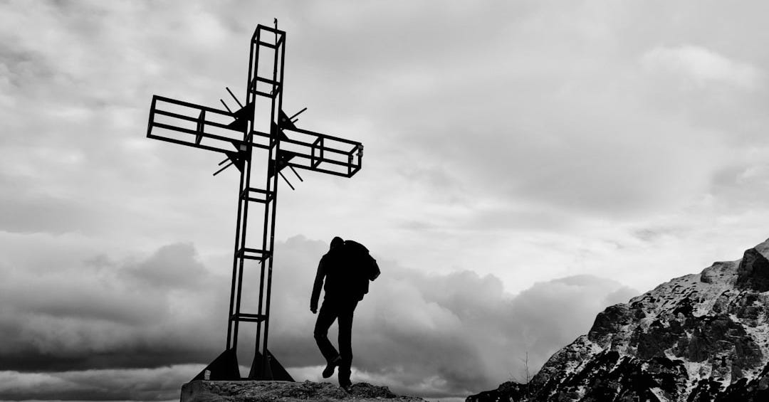 a man standing on top of a mountain next to a cross