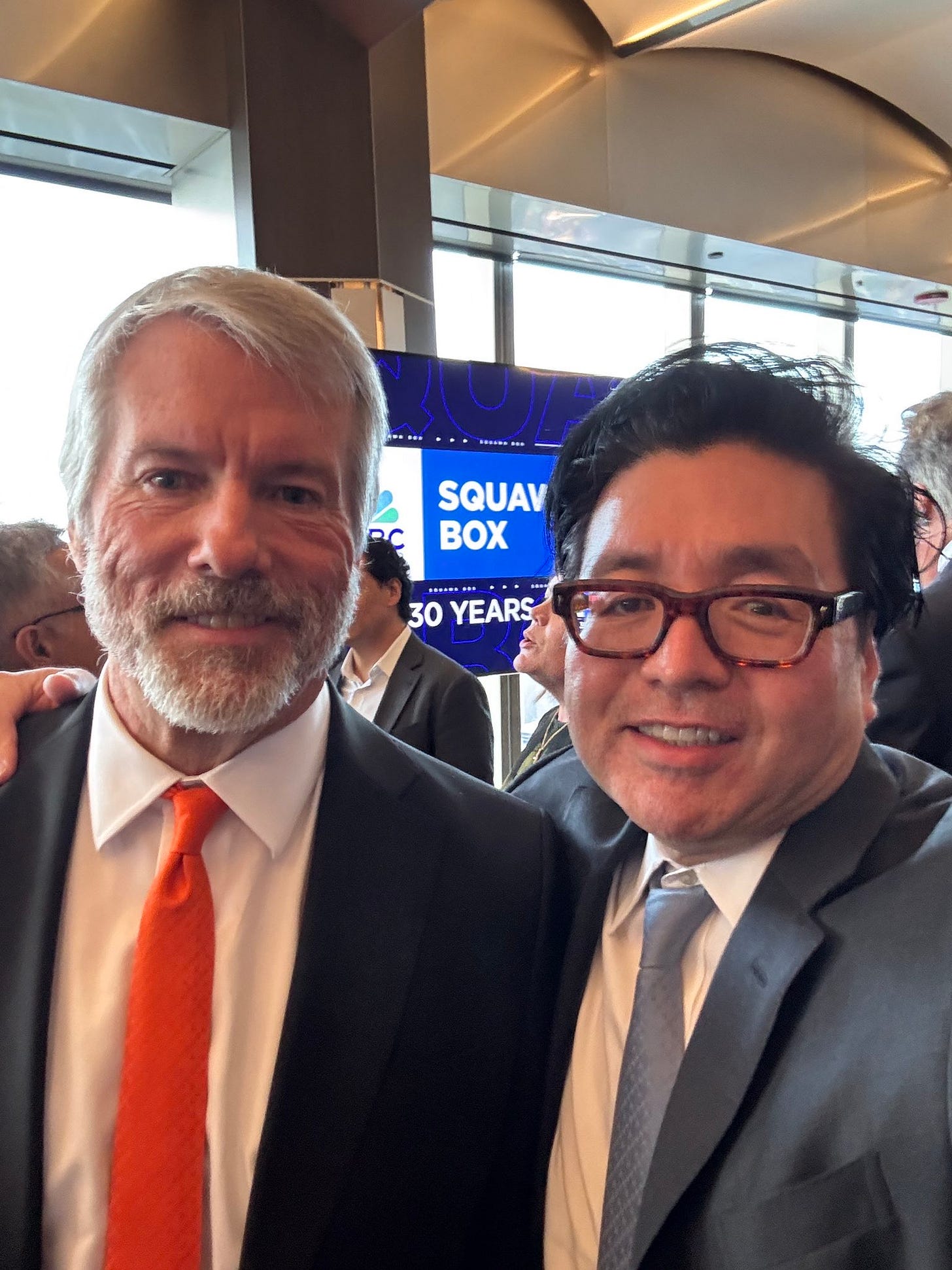 Two men in suits stand side by side in a modern conference room with large windows and a curved ceiling one with gray hair and beard wearing a white shirt orange tie and dark jacket the other with black hair glasses and smiling expression wearing a white shirt light blue tie and gray jacket a blue banner in background reads SQUARE 30 YEARS with white text SQAVC. Two men in suits stand side by side in a modern conference room with large windows and a curved ceiling one with gray hair and beard wearing a white shirt orange tie and dark jacket the other with black hair glasses and smiling expression wearing a white shirt light blue tie and gray jacket a blue banner in background reads SQUARE 30 YEARS with white text SQAVC.