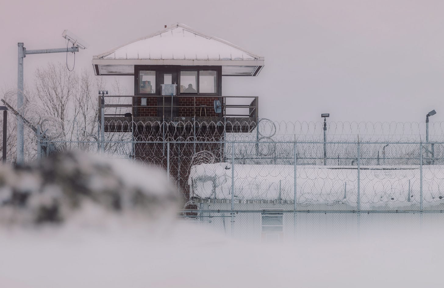 A faded black-and-white image of prison gates in snow A faded black-and-white image of prison gates in snow