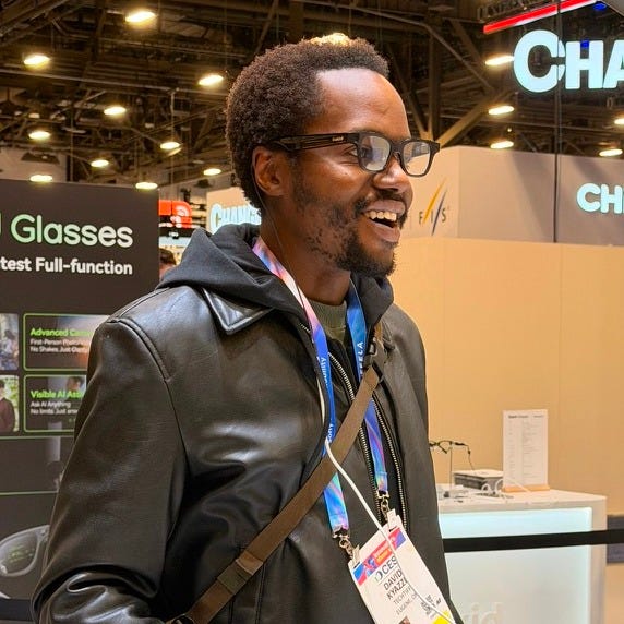 A man wearing glasses and a leather jacket smiles while standing on the CES show floor, with AR glasses signage and expo booths visible in the background. A man wearing glasses and a leather jacket smiles while standing on the CES show floor, with AR glasses signage and expo booths visible in the background.