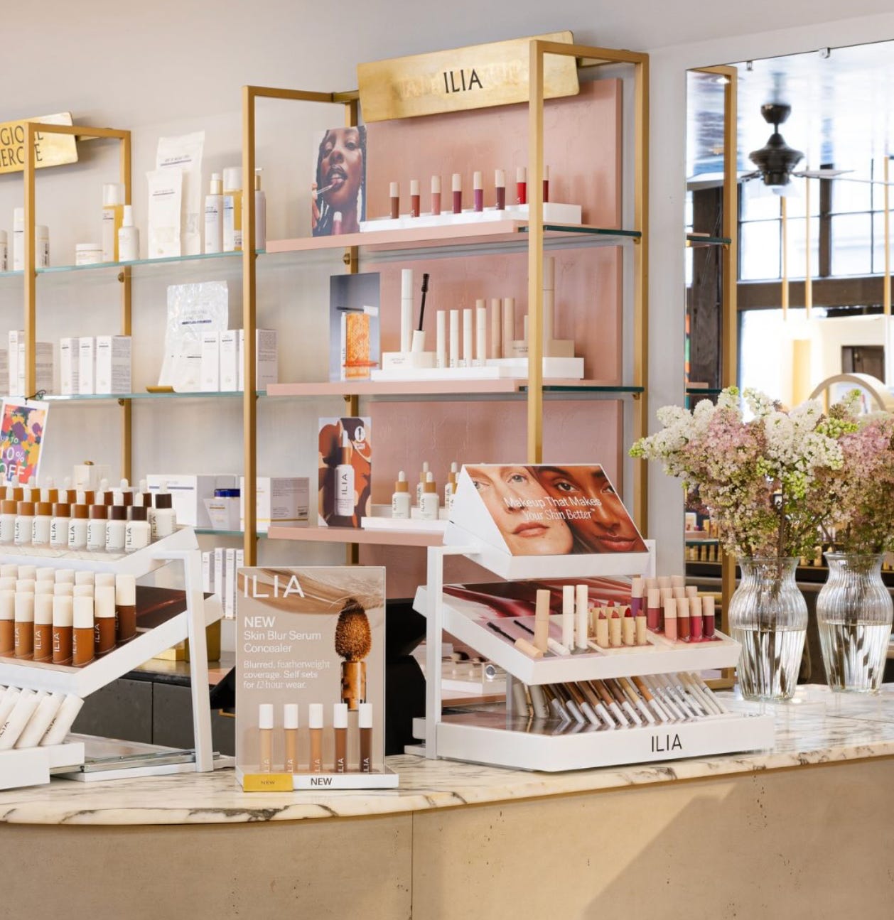 The modern ILIA Beauty retail counter inside Liberty London, featuring a range of skin-first complexion products, blushes, and serums displayed on marble and gold shelving.