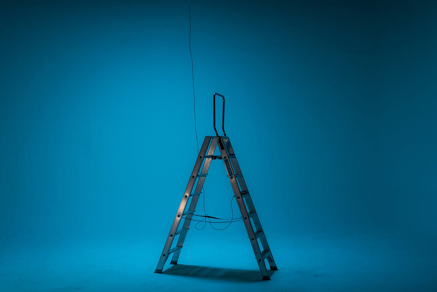 A stepladder standing under an unconnected wire in a blue-lit room – staged and ready, but unfinished.